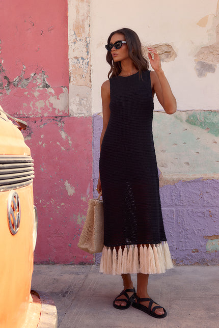 Woman in a black dress with beige hem standing in front of a colorful wall.