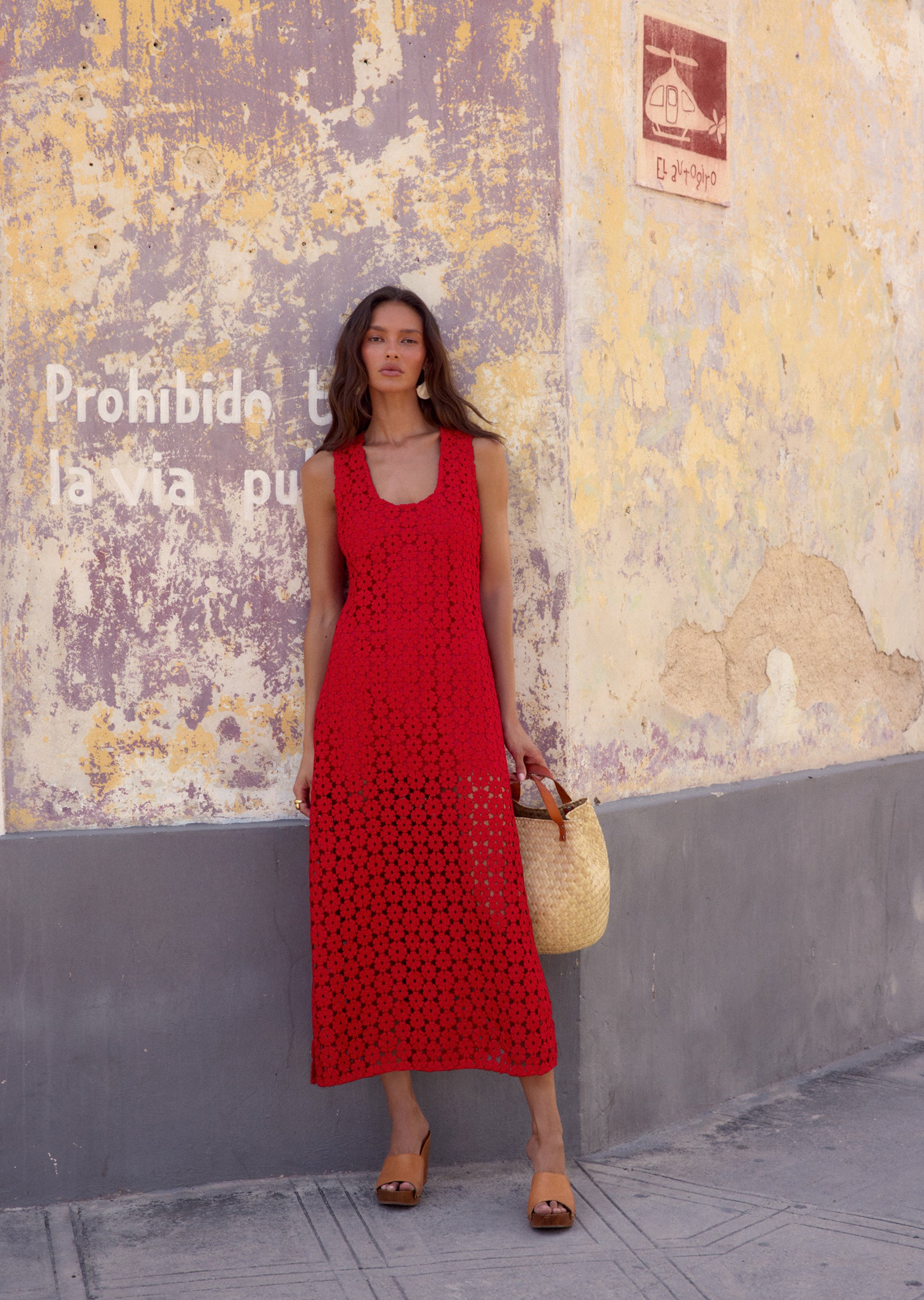 Woman in a red dress standing against a textured wall with graffiti.