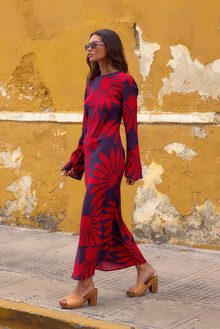 Woman in a red and blue patterned dress walking against a yellow wall.