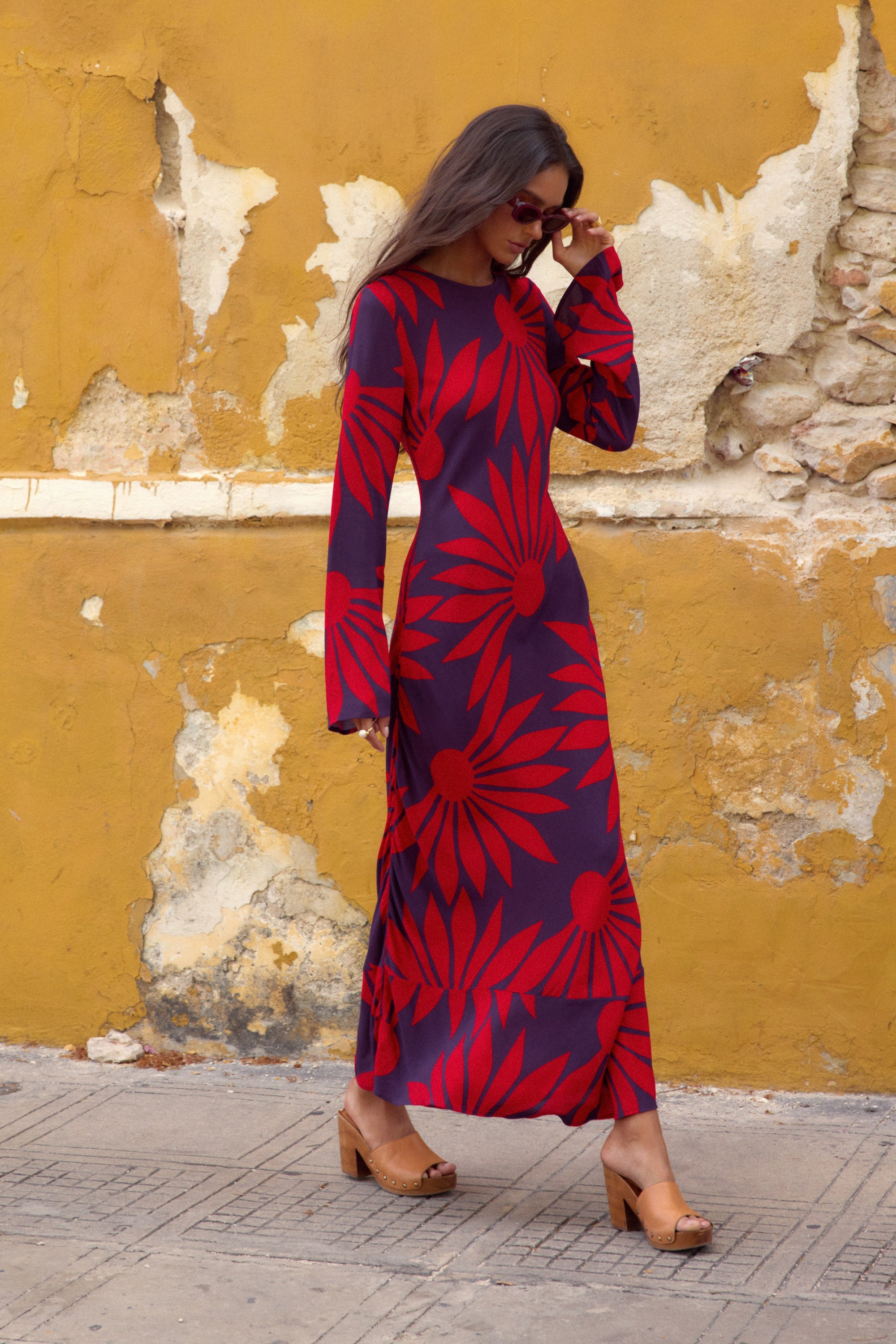 Woman wearing a red and blue patterned dress against a yellow wall.